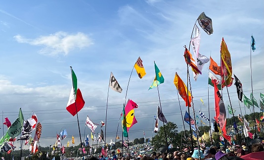 Glastonbury Festival, Pilton, Somerset, UK - June 23, 2023: A sea of festival flags flying high above the crowds at the Pyramid stage.  Personalised flags have become very popular with festival goers at Glastonbury. They are a good way to pinpoint your friends in the vast crowds. They are also used within the busy camp sites to be able to find your tent easily.