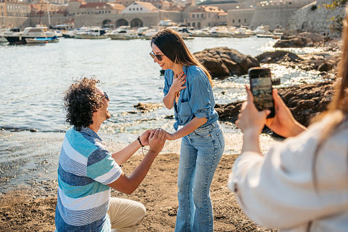 Young woman filming her male friend proposing to his girlfriend in Dubrovnik Old Town bay in Croatia.