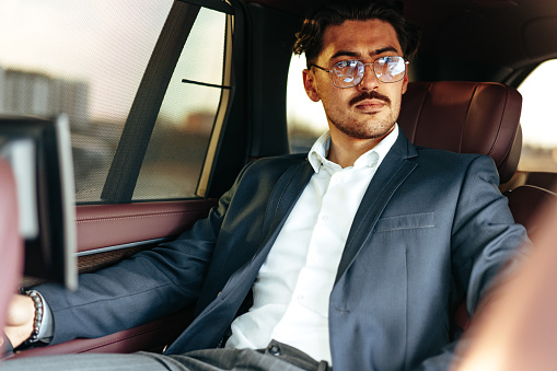 Young businessman in suit and glasses sitting on passenger seat in a luxury car close up
