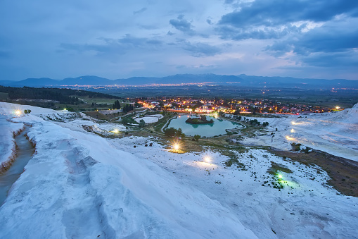 Pamukkale travertines in foreground. Sunset sky and illuminated houses in background.
