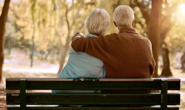 Photo of Love, hug and old couple in a park on a bench for a calm, peaceful or romantic summer marriage anniversary date. Nature, romance or back view of old woman and elderly partner in a relaxing embrace