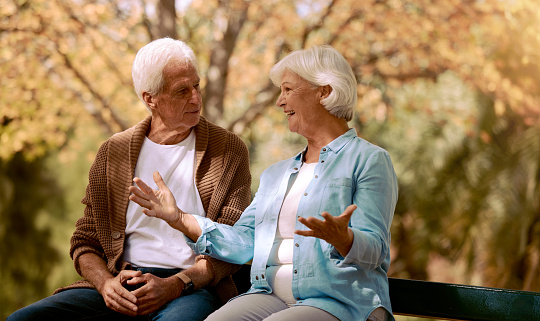 Nature, park and retirement with a senior couple sitting together on a wooden bench outdoor in a garden. Spring, love and summer with a mature man and woman bonding outside in the countryside