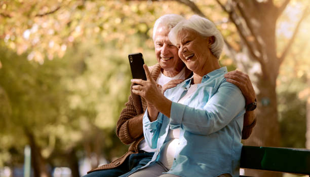 älteres paar, selfie und lächeln im park, glücklich und bäume durch verschwommenen hintergrund für soziale medien. älterer mann, alte frau und smartphone auf parkbank für glücksfoto, liebe oder videoanruf in quebec - senior adult women park bench 70s stock-fotos und bilder