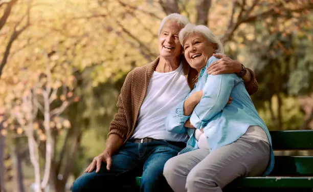 Photo of Senior couple, park bench and happy while sitting together in retirement for freedom, peace and calm with a smile and happiness in nature. Old man and woman outdoor to relax while on vacation