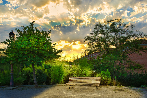 Wooden bench in a park with dramatic sky in the background at sunrise.
