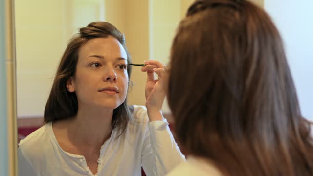 Young Woman Putting On Eyebrow Pencil In A Bathroom Mirror