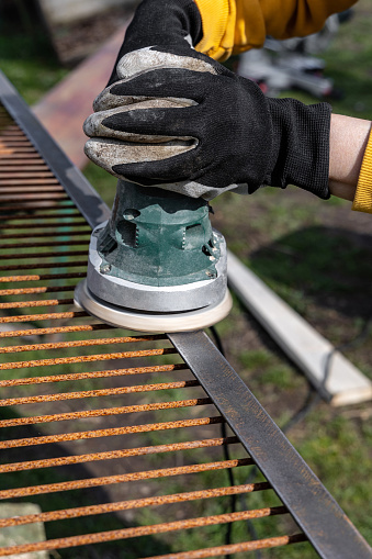 Grinding a new rusty metal grate with a vibrating sander