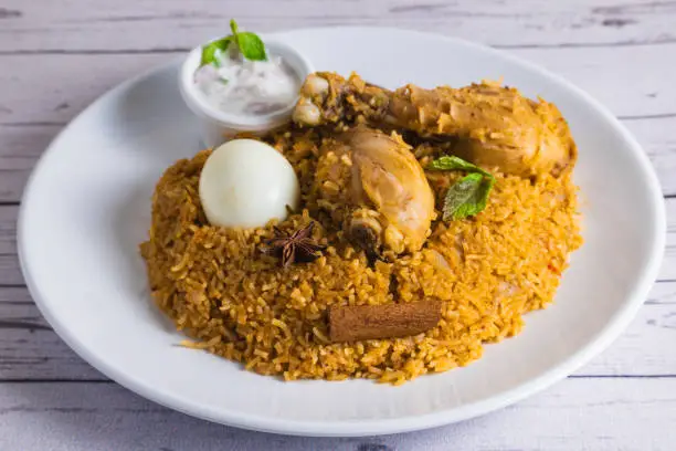 Delicious chicken biriyani on a white plate. Indian style chicken biryani with egg and yogurt.