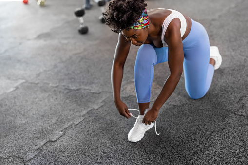 African female sportswoman is tying shoelaces in a modern gym.