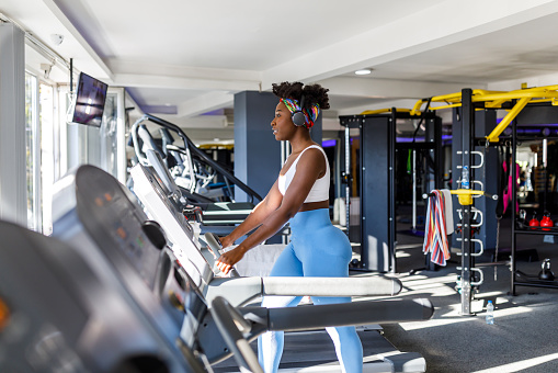 A female African-American athlete is exercising in a modern gym on a treadmill and listening to music.