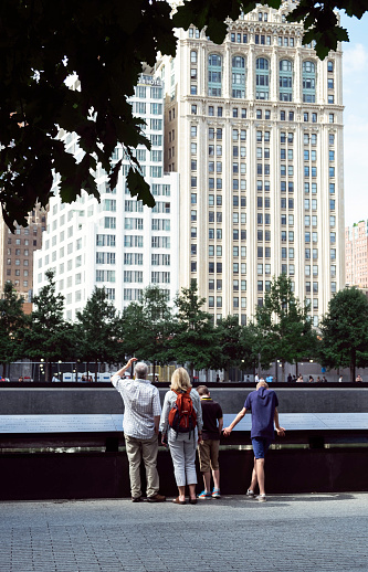 Lower Manhattan, New York - July 10, 2015: A family of four stands in front of one of the waterfalls as part of a tribute to the victims of the 9/11 attacks. The man looks up at the skyscrapers as the two children look at the names on the surrounding wall of the waterfall.