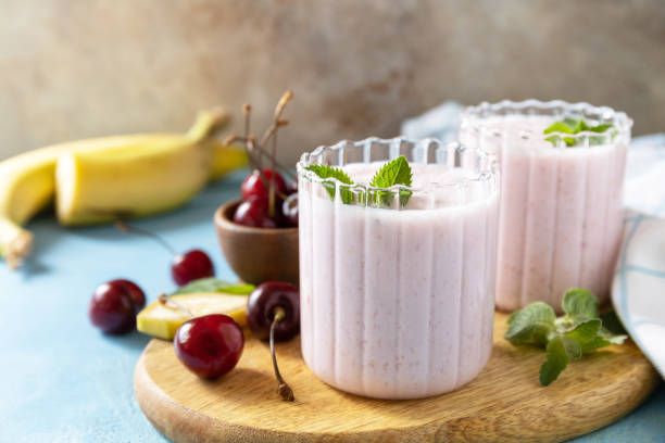 frische saisonale smoothies. smoothies mit süßkirsche und banane mit joghurt auf holzbrett auf steinernem hintergrund. - healthy lifestyle cranberry healthy eating milk shake stock-fotos und bilder