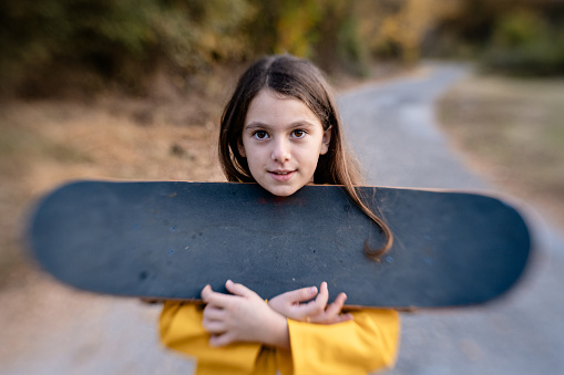 Girl posing with skateboard on a road with dry autumn leafs