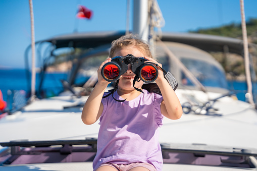 Little girl on a yacht looking through binoculars in the sea. High quality photo
