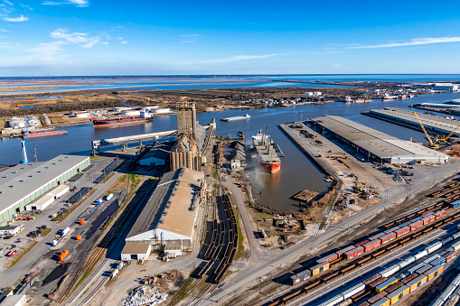 Mobile, United States - January 31, 2022:  A transport ship being loaded for export along the river just north of downtown Mobile, Alabama with the railyards in the foreground shot from an altitude of about 600 feet.