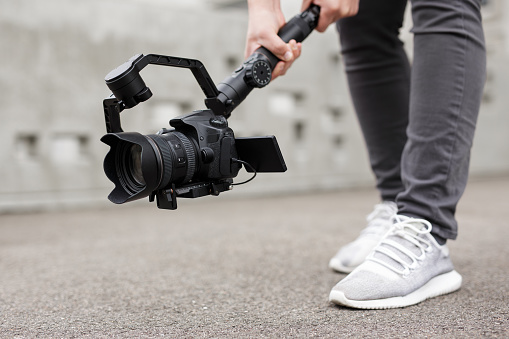 videography, filmmaking and creativity concept - close up of modern dslr camera on 3-axis gimbal stabilizer in male hands over grey background