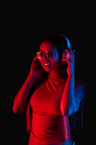 asian female woman with heart shaped sunglasses listening to music with headphones in studio with red light
