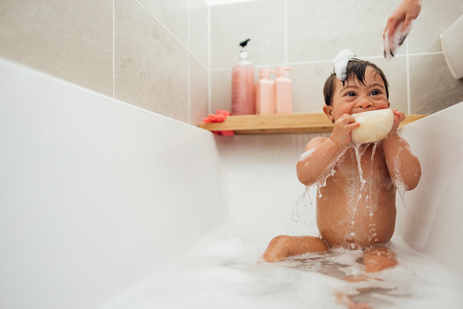 Front-view of a young male toddler who has down syndrome having a bubble bath in the bathtub at his home in Ashington, England.