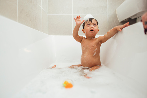 Front-view of a young male toddler who has down syndrome having a bubble bath in the bathtub at his home in Ashington, England.