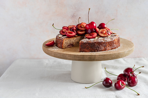 Round cherry almond cake dusted with podered sugar served on cake stand, table front view on light background