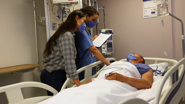 Nurse talking to a woman visiting a mature male patient in the ICU at the hospital