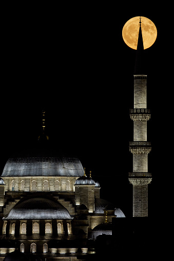 Historic mosque with lights at night and full moon at top of the minaret surrounding the crescent
