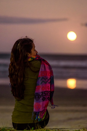 Young woman watching the full moon over the sea at Peruibe beach on the southeast coast of Brazil
