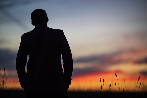 Young man standing on a hill watching the sunset