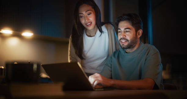 istock Portrait of Young Couple Using Laptop Computer While Sitting in the Kitchen at Home. Happy Excited Couple Opening their Own Small Business for E-Commerce and Receiving their First Orders. 1514023495