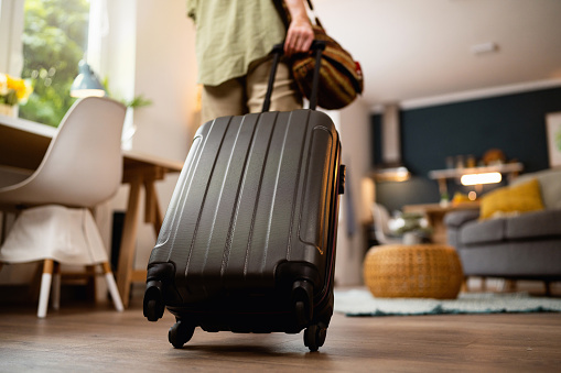 Rear-view of an unrecognizable woman pulling suitcase into apartment