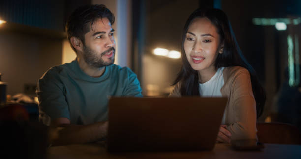 istock Portrait of Young Couple Using Laptop Computer While Sitting in the Kitchen at Home. Engaged Couple Doing e-Shopping for their Wedding Preparations, Discussing Different Options Using Technology. 1514024566