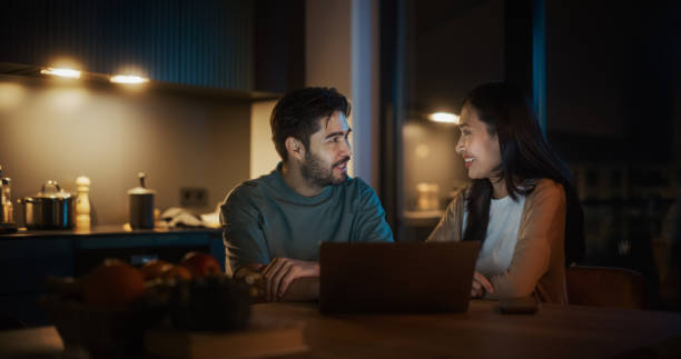istock Portrait of Young Couple Using Laptop Computer While Sitting in the Kitchen at Home. Engaged Couple Doing Online Shopping for their Wedding Preparations, Discussing Different Options Using Technology 1514025101