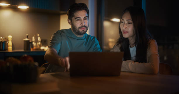 istock Portrait of a Young Couple Using a Laptop Computer While Sitting in the Kitchen at Home. Newly Married Husband and Wife Checking Real Estate Market to Find Their Future Home, Discussing Possibilities 1514025621