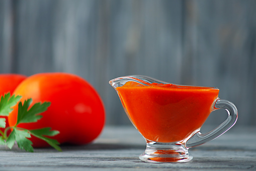 Close-up of homemade ketchup and tomatoes with parsley on a gray wooden background.