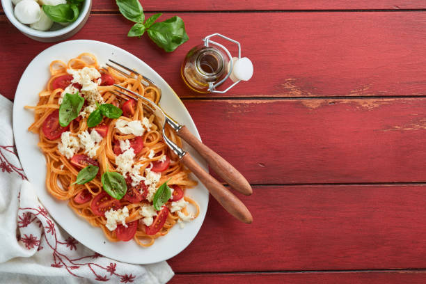 salat-caprese oder pasta-spaghetti gebrochen mit basilikum und mozzarella ala caprese auf einem weißen teller auf rotem rustikalem holzhintergrund. traditionelle italienische küche. italienisches food-konzept. draufsicht. - caprese salad antipasto wine mozzarella stock-fotos und bilder