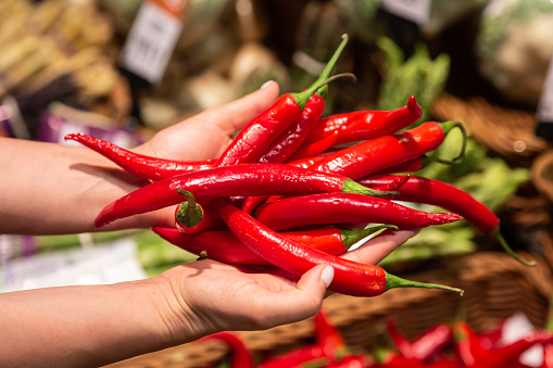 Woman chooses red chilli, buying vegetables in supermarket. Concept of shopping groceries and healthy lifestyle.