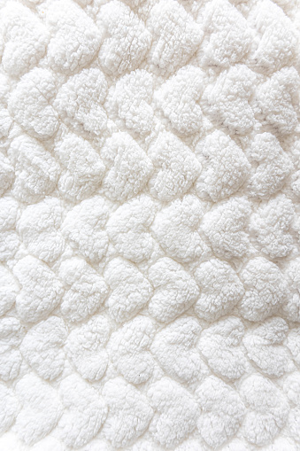 Close-up white texture of a blanket for a baby, a soft blanket with a pattern of hearts, top view.