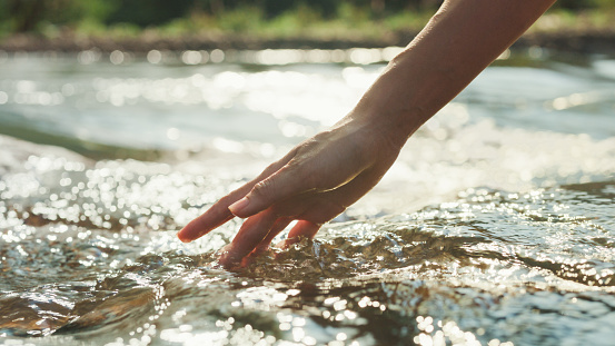 Closeup hand woman touching water in the forest river in vacation with camping at morning. Lifestyle travel nature concept.