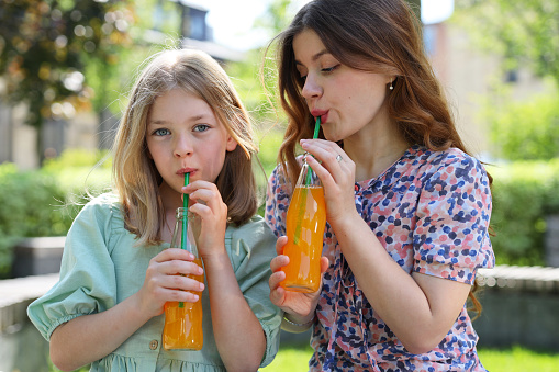 Little girl and woman with summer cold drinks in the park.