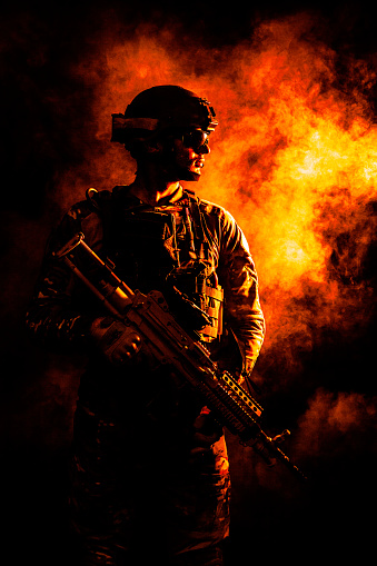 Backlit silhouette of special forces marine  on fire explosion background. Battle, bombs exploding, smoke billows