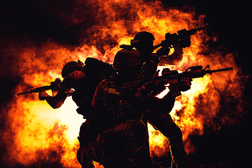 Backlit silhouette of special forces operators fighting in the smoke on fire explosion background. Battle, bombs exploding, they fighting no matter what