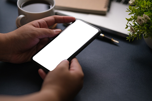 Over shoulder view of woman holding smart phone while sitting at her workspace.