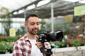 Video operator with a gimbal and mirrorless recording video in greenhouse site, smiling with plaid shirt