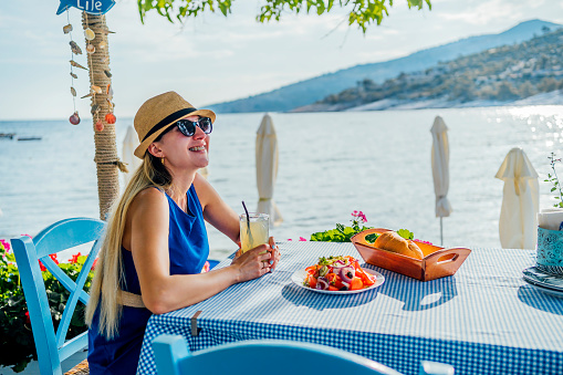 Young cheerful woman enjoying Mediterranean food during vacation on a sunny summer day by the sea