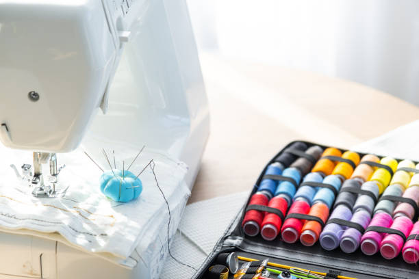 istock Sewing layout with multicolored spools of thread close-up, needles, electric sewing machine. Filling the thread into the sewing needle, adjusting the tension. hobby, home business 1514288261
