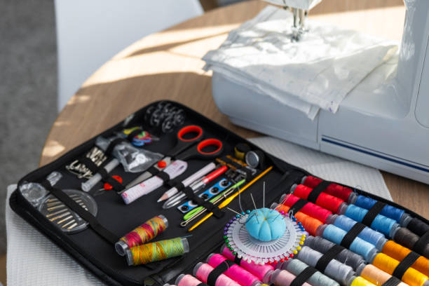 istock Sewing layout with multicolored spools of thread close-up, needles, electric sewing machine. Filling the thread into the sewing needle, adjusting the tension. hobby, home business 1514288266