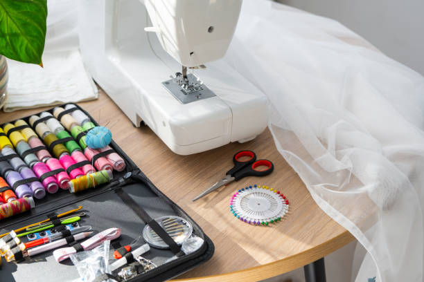 istock Sewing layout with multicolored spools of thread close-up, needles, electric sewing machine. Filling the thread into the sewing needle, adjusting the tension. hobby, home business 1514288638