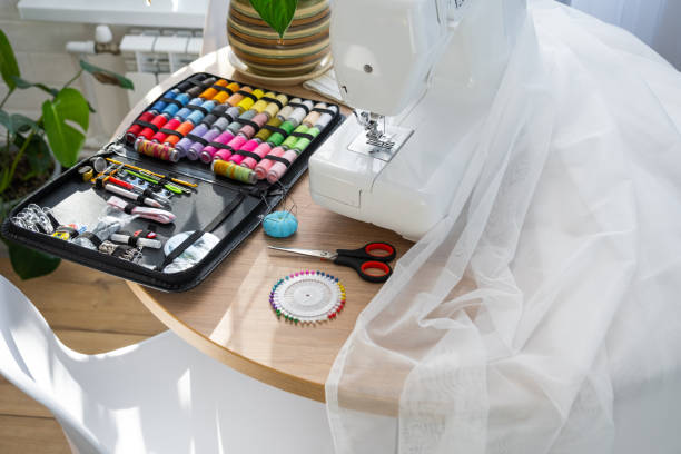 istock Sewing layout with multicolored spools of thread close-up, needles, electric sewing machine. Filling the thread into the sewing needle, adjusting the tension. hobby, home business 1514288784