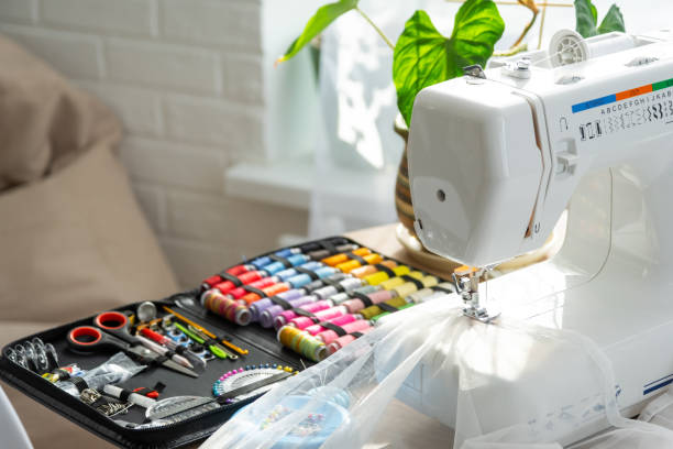 istock Sewing layout with multicolored spools of thread close-up, needles, electric sewing machine. Filling the thread into the sewing needle, adjusting the tension. hobby, home business 1514288788
