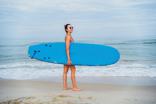 Young cheerful woman on the beach with her surfboard